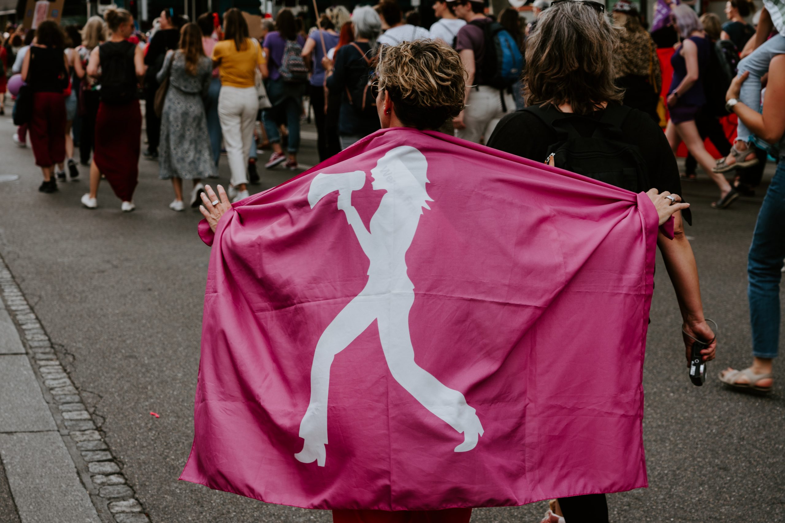 Mulher durante protesto em Zurich, envolta em uma bandeira cor de rosa, com uma ilustração de mulher com megafone. Sobre igualdade feminina