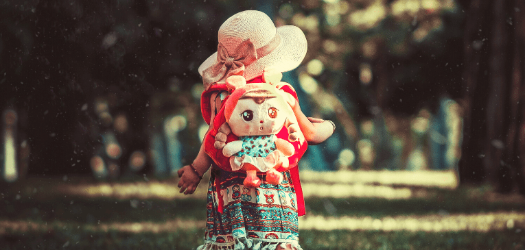 Imagem ilustrativa para falar de retrospectiva. Uma menina com uma mochila de boneca caminhando em um lugar gramado. Sobre redescobrir nossa missão.